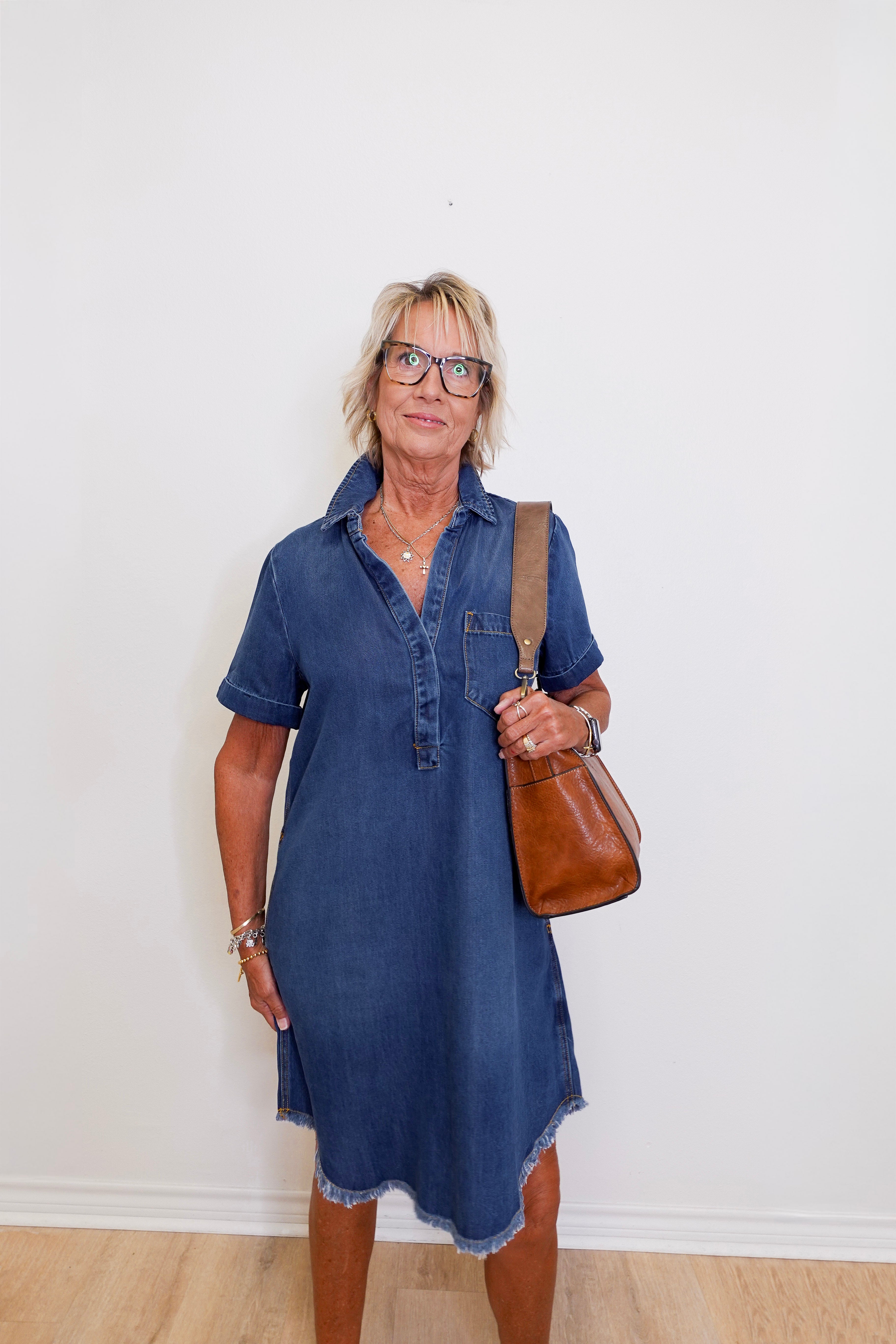 Woman wearing a blue popover shirt dress with pockets in front a white background. 