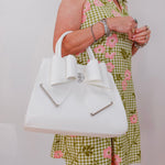Woman in a green floral dress holding a white handbag with a bow.