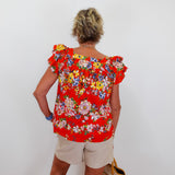 Person wearing a red floral blouse and beige shorts against a white wall.