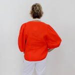 Person wearing an orange top and white pants against a plain background
