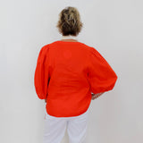 Person wearing an orange top and white pants against a plain background
