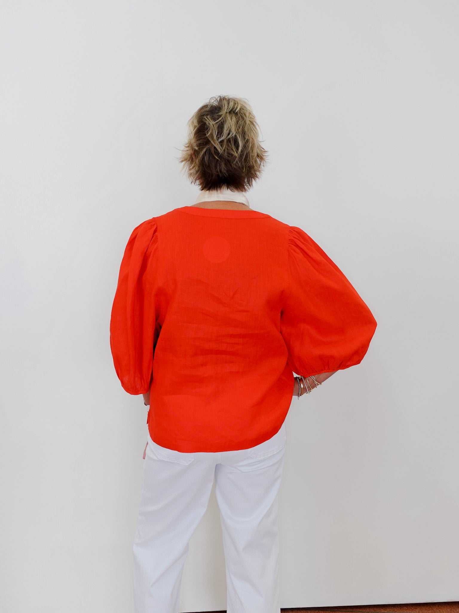 Person wearing an orange top and white pants against a plain background