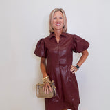 Woman wearing a brown leather dress with puff sleeves against a white wall.