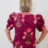 Person wearing a burgundy blouse with floral patterns against a white background