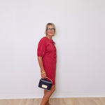 Woman in a red dress holding a blue handbag against a white wall.