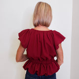 Person wearing a red blouse with ruffled sleeves against a white background