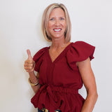 Woman wearing a red blouse with ruffled details, giving a thumbs-up gesture against a plain background.