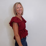 Woman wearing a red blouse and blue jeans against a white wall