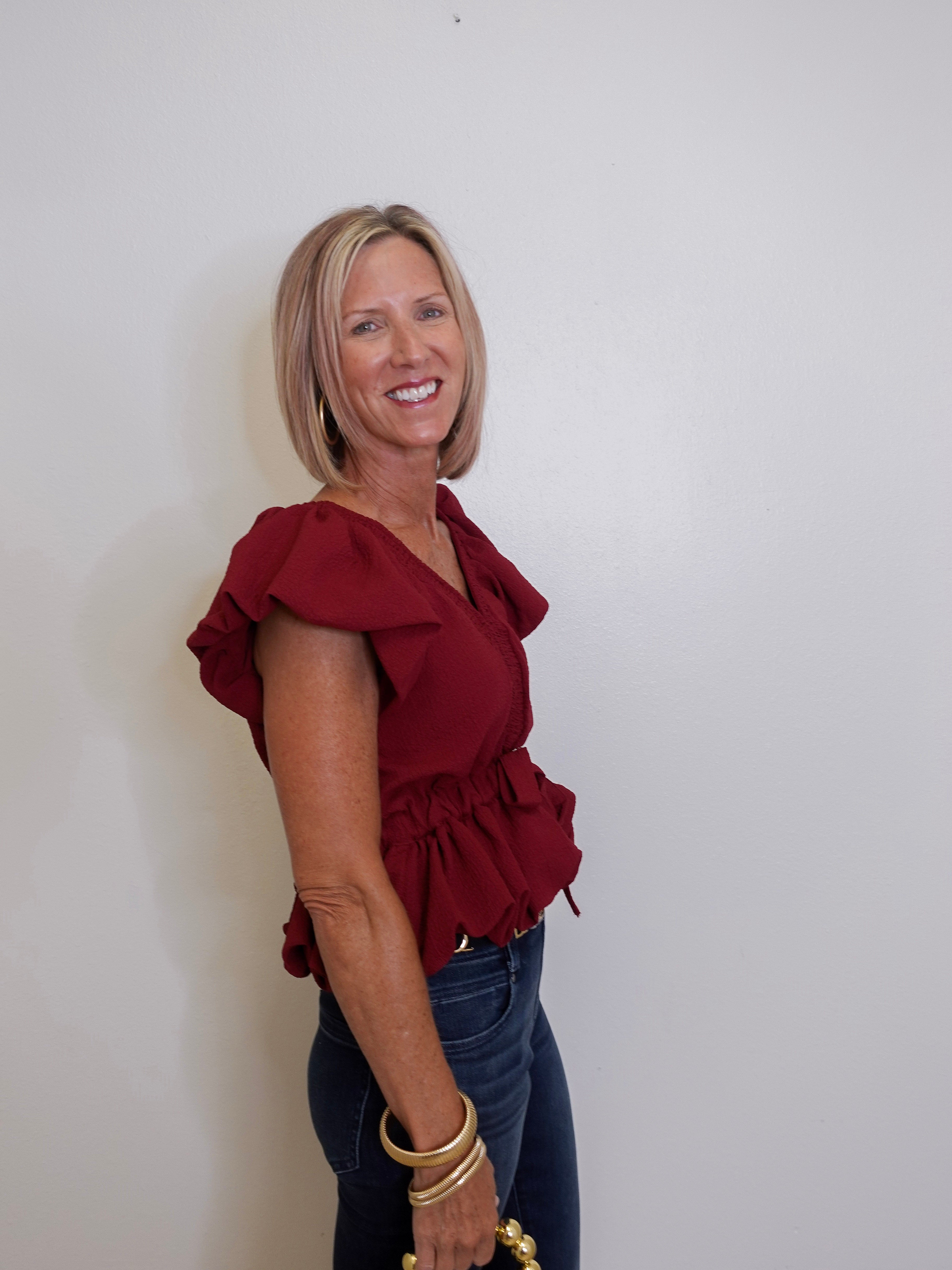 Woman wearing a red blouse and blue jeans against a white wall