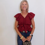 Woman wearing a red blouse and blue jeans, holding a leopard print bag against a white background
