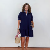 Woman wearing a navy dress with a white wall background