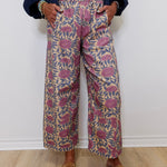 Person wearing patterned pants and brown loafers against a white wall.