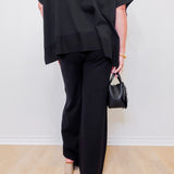 Person wearing a black outfit with wide-leg pants and holding a small black handbag against a white background.