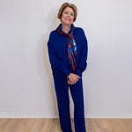 Person wearing a blue outfit with a patterned scarf against a white wall.