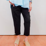 Person wearing a light blue top, black pants, and beige sandals on a plain background