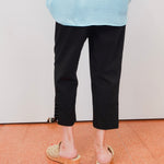Person wearing a light blue shirt, black pants, and sandals on a plain background