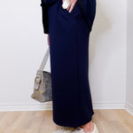 Person wearing navy pants and white sneakers against a white wall.