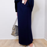 Person wearing navy pants and white sneakers against a white wall.