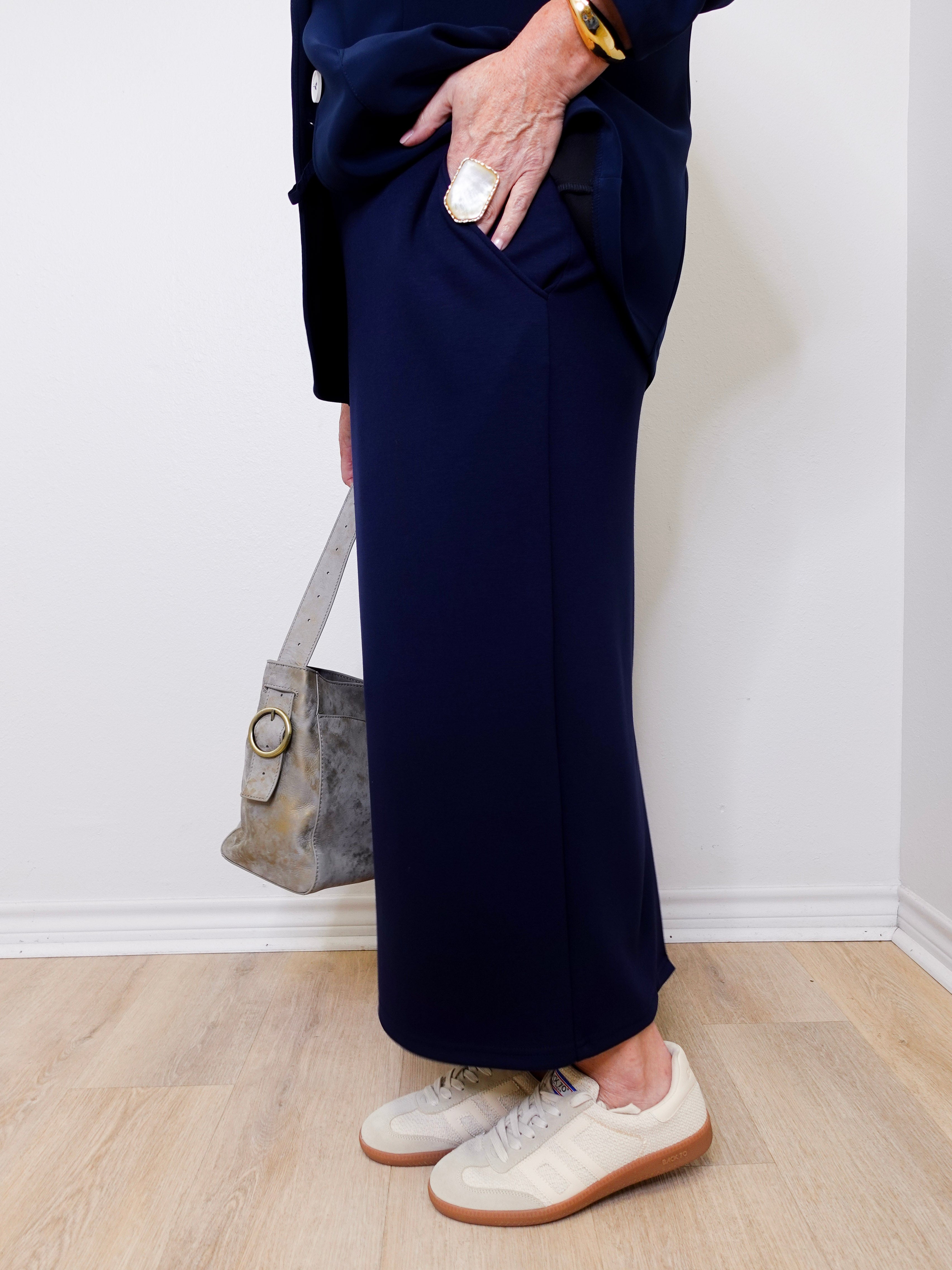 Person wearing navy pants and white sneakers against a white wall.