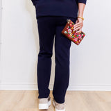 Person wearing navy blue pants and holding a colorful floral clutch against a white background