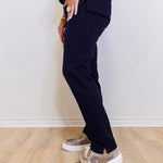 Person wearing navy blue pants and patterned sneakers on a light wooden floor.