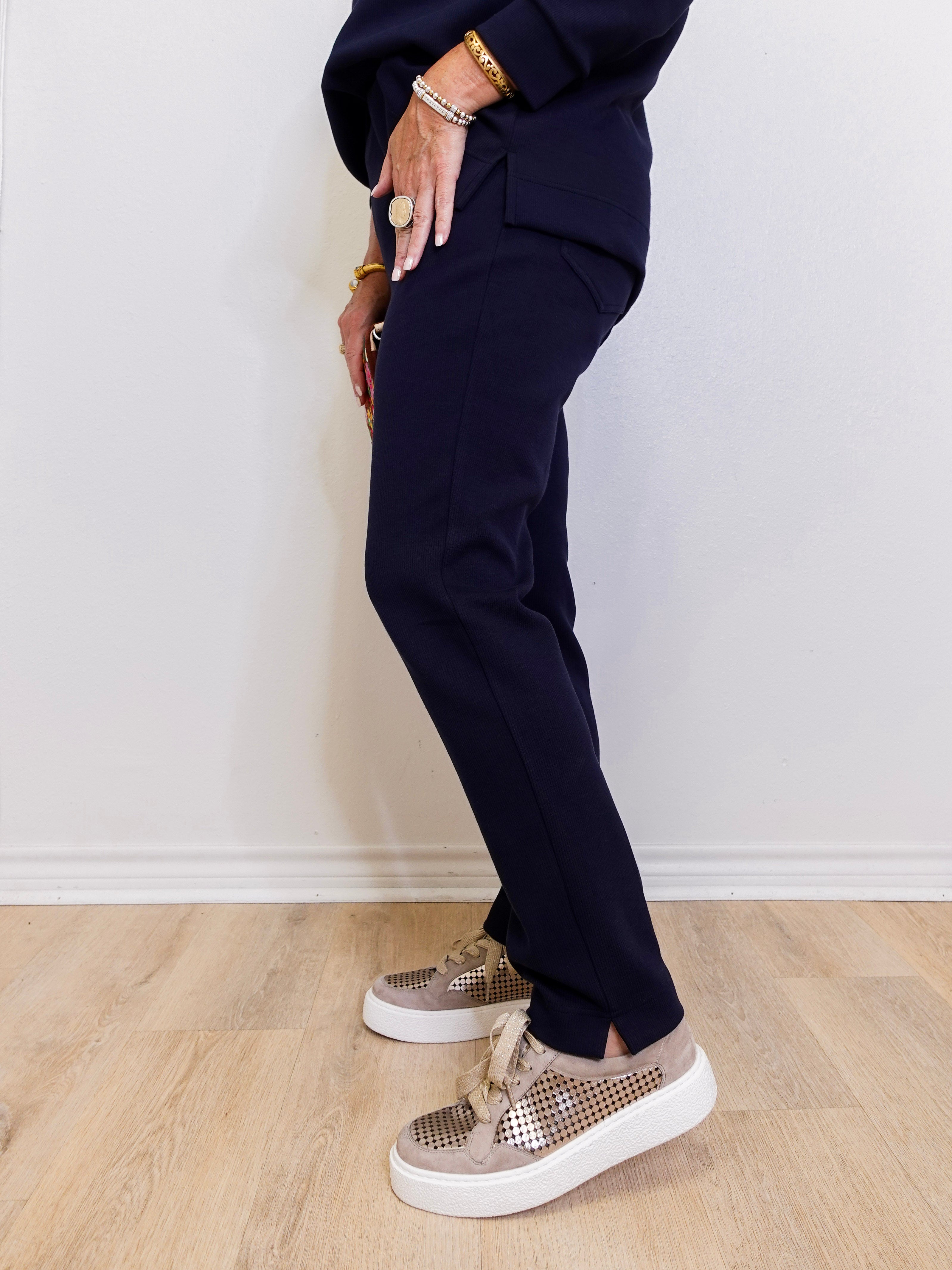 Person wearing navy blue pants and patterned sneakers on a light wooden floor.