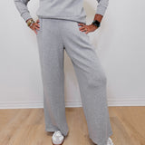 Person wearing a gray sweatshirt and pants with white sneakers on a wooden floor.