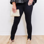 Person wearing black leggings and a leather jacket, holding a beige clutch against a white background.
