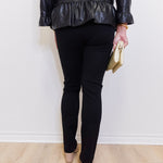Person wearing a black leather jacket and black pants against a white wall.