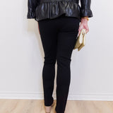 Person wearing a black leather jacket and black pants against a white wall.