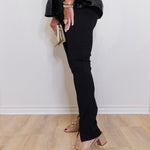 Person wearing black pants and beige heels against a white wall.