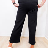 Person wearing black pants and white shoes on a light wooden floor.