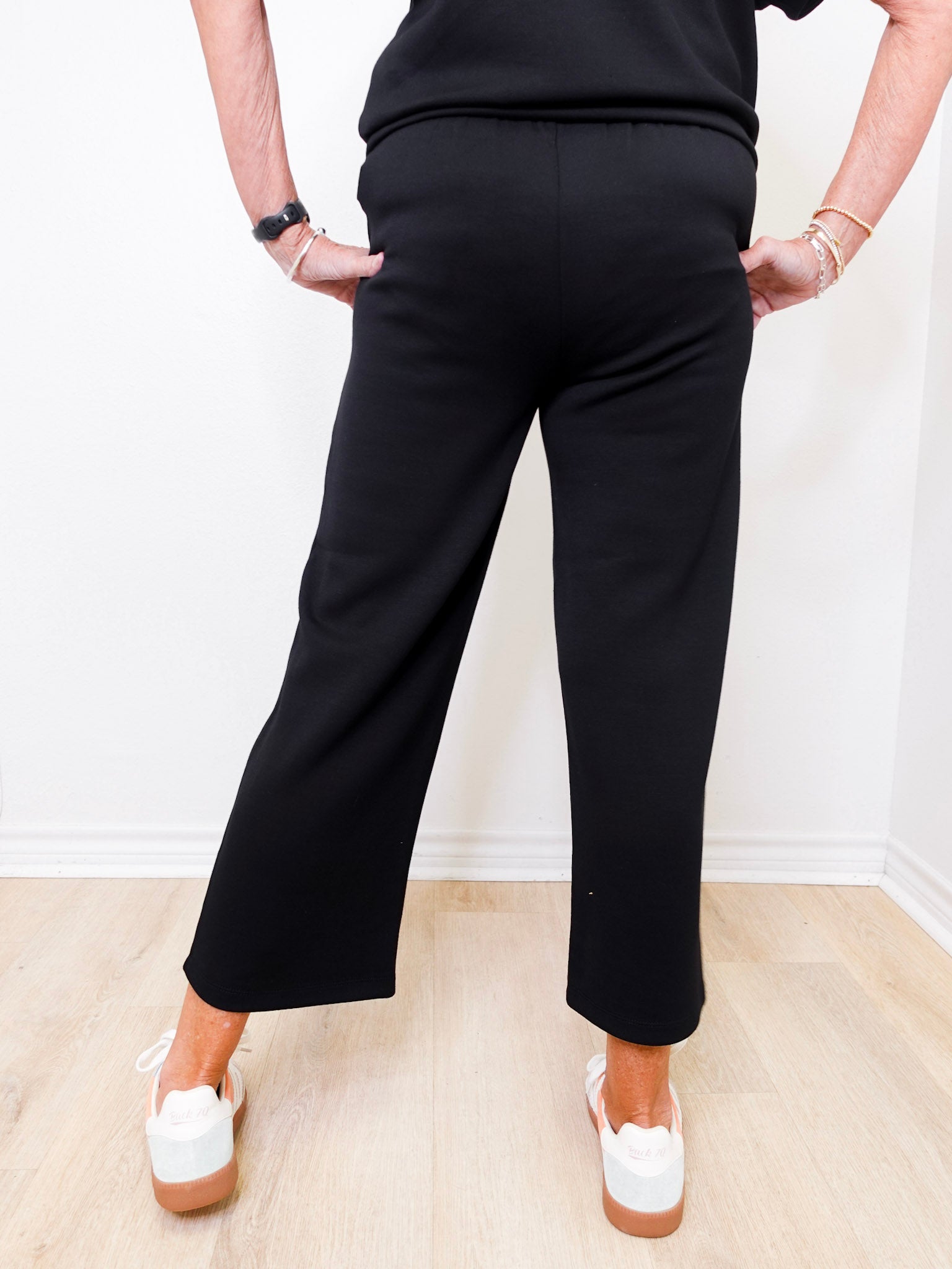 Person wearing black pants and white shoes on a light wooden floor.