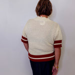 Person wearing a cream sweater with red stripes against a white wall