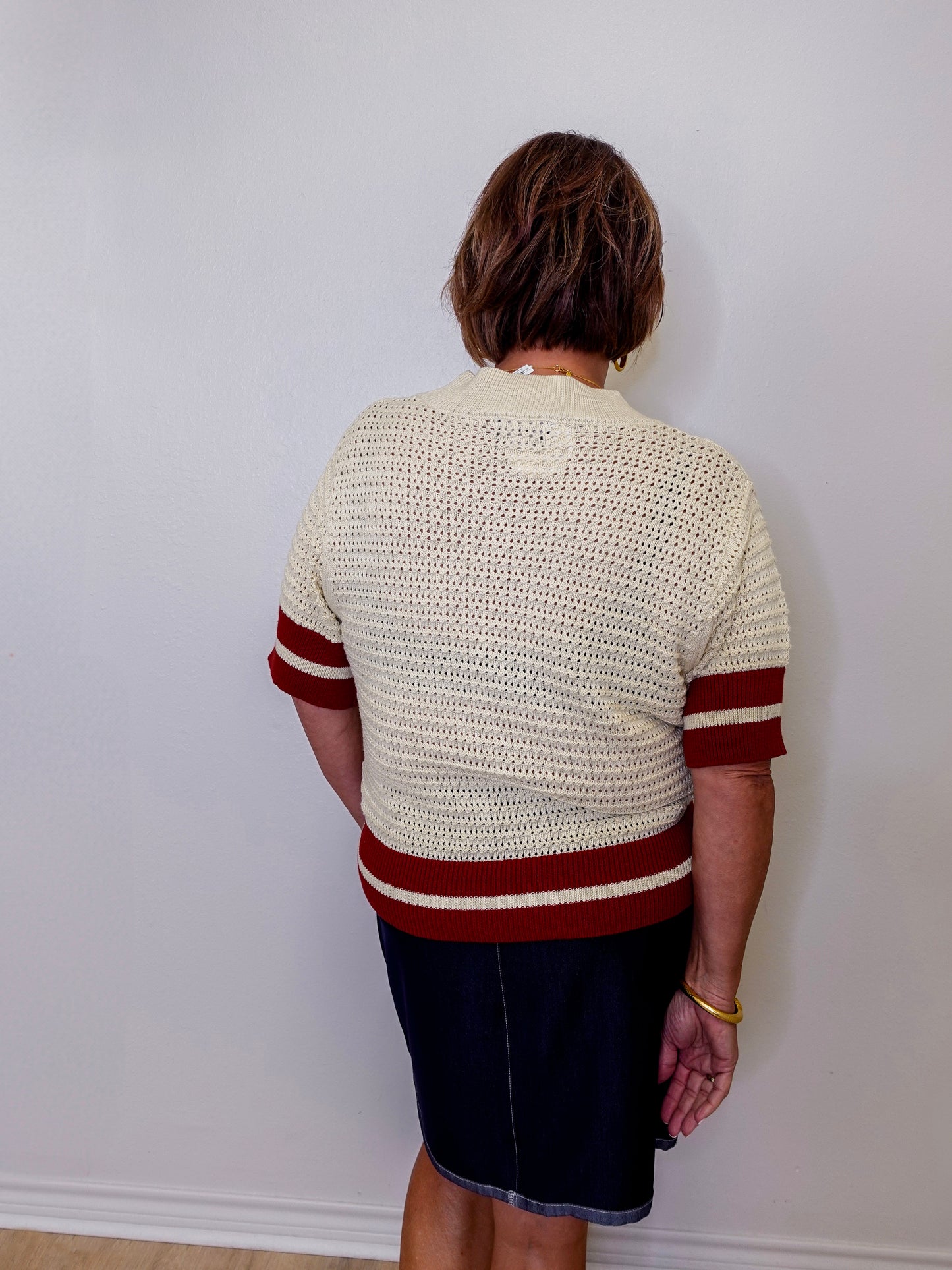 Person wearing a cream sweater with red stripes against a white wall