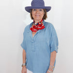 Woman wearing a blue hat and light blue shirt with a red scarf, standing against a white background