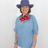 Woman wearing a blue hat and light blue shirt with a red scarf, standing against a white background
