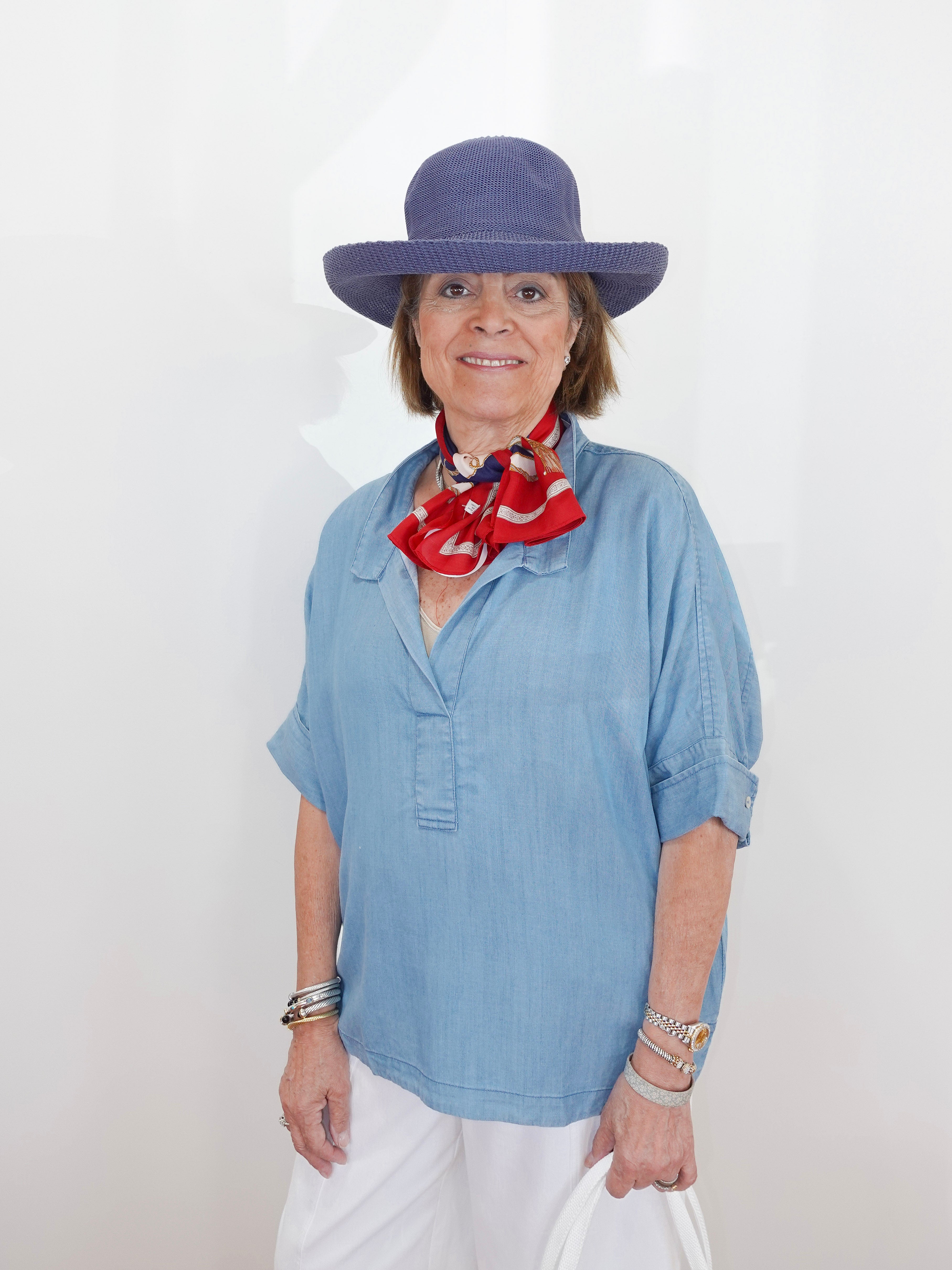 Woman wearing a blue hat and light blue shirt with a red scarf, standing against a white background