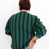 A person shown from the back wearing a dark green and black vertically striped long-sleeve top with light blue jeans, set against a plain white background.