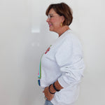 A woman in profile wearing a light gray crewneck sweatshirt and light blue jeans, standing against a plain white wall.