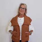 Woman wearing a brown vest over a white sweater on a plain background