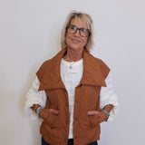 Woman wearing a brown vest over a white sweater on a plain background