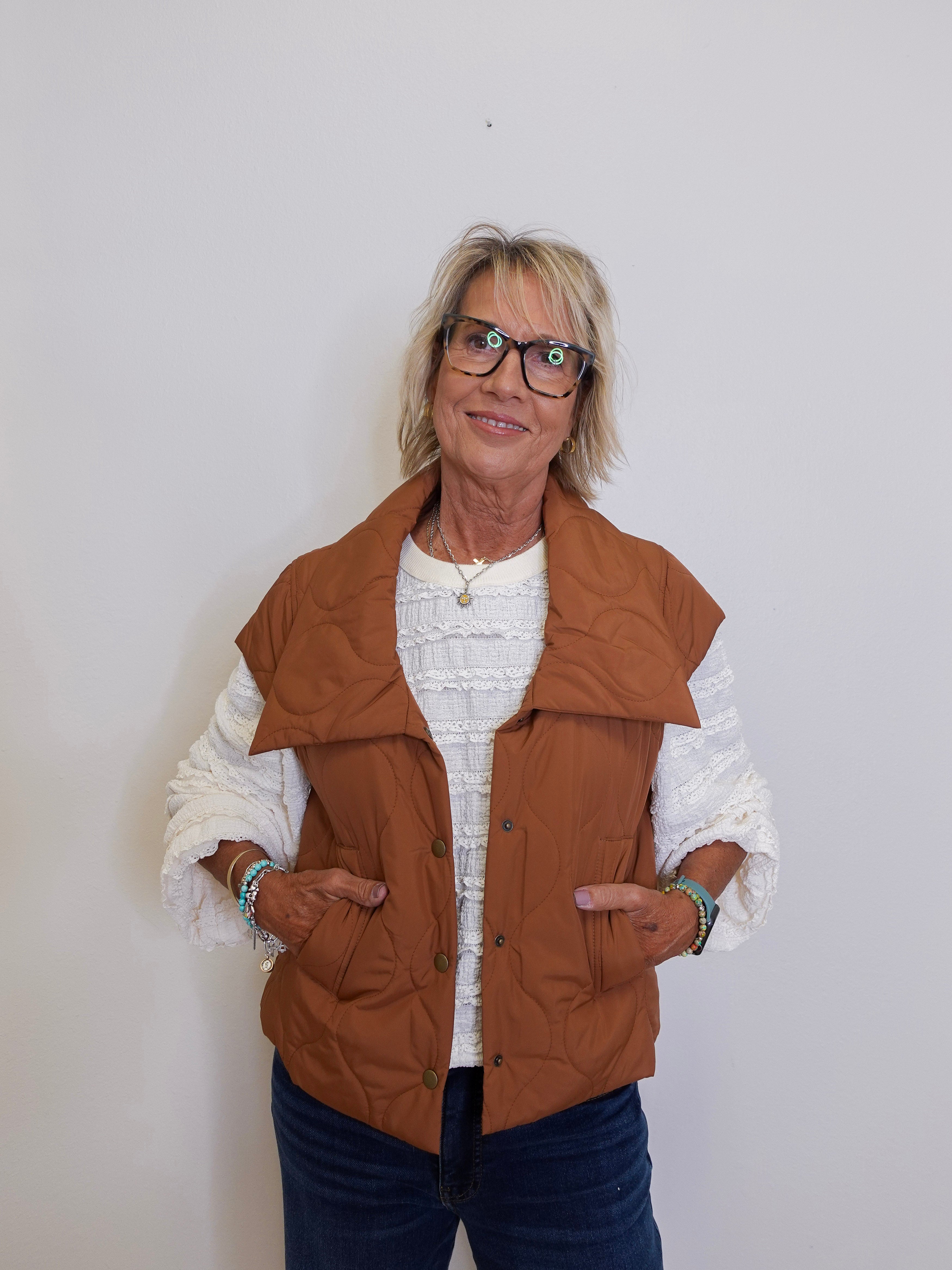 Woman wearing a brown vest over a white sweater on a plain background