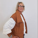 Woman wearing a brown jacket with white ruffled sleeves against a plain background