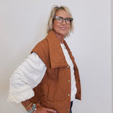 Woman wearing a brown jacket with white ruffled sleeves against a plain background