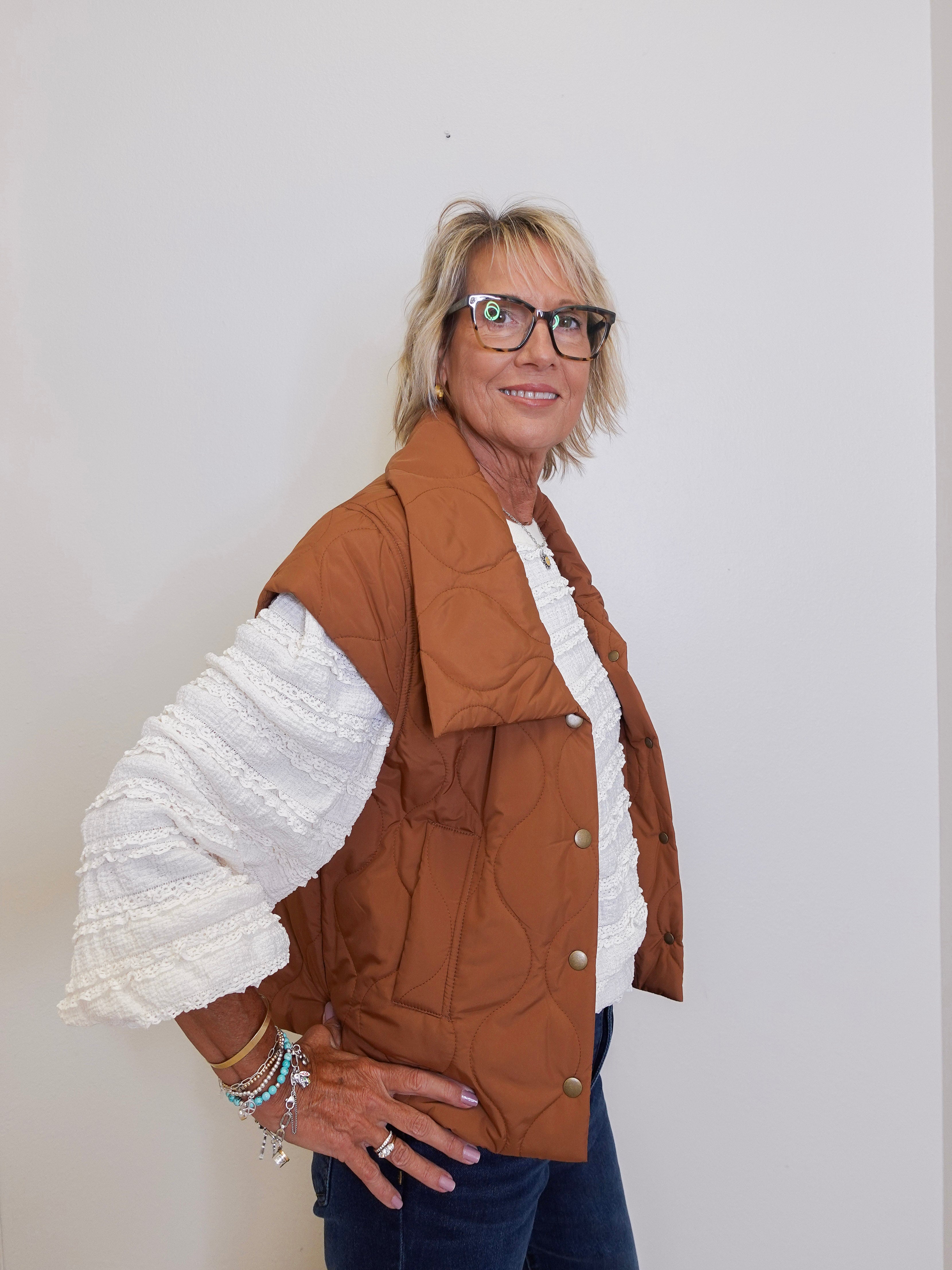 Woman wearing a brown jacket with white ruffled sleeves against a plain background