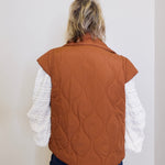 Person wearing a brown quilted vest over a white long-sleeve shirt against a plain background