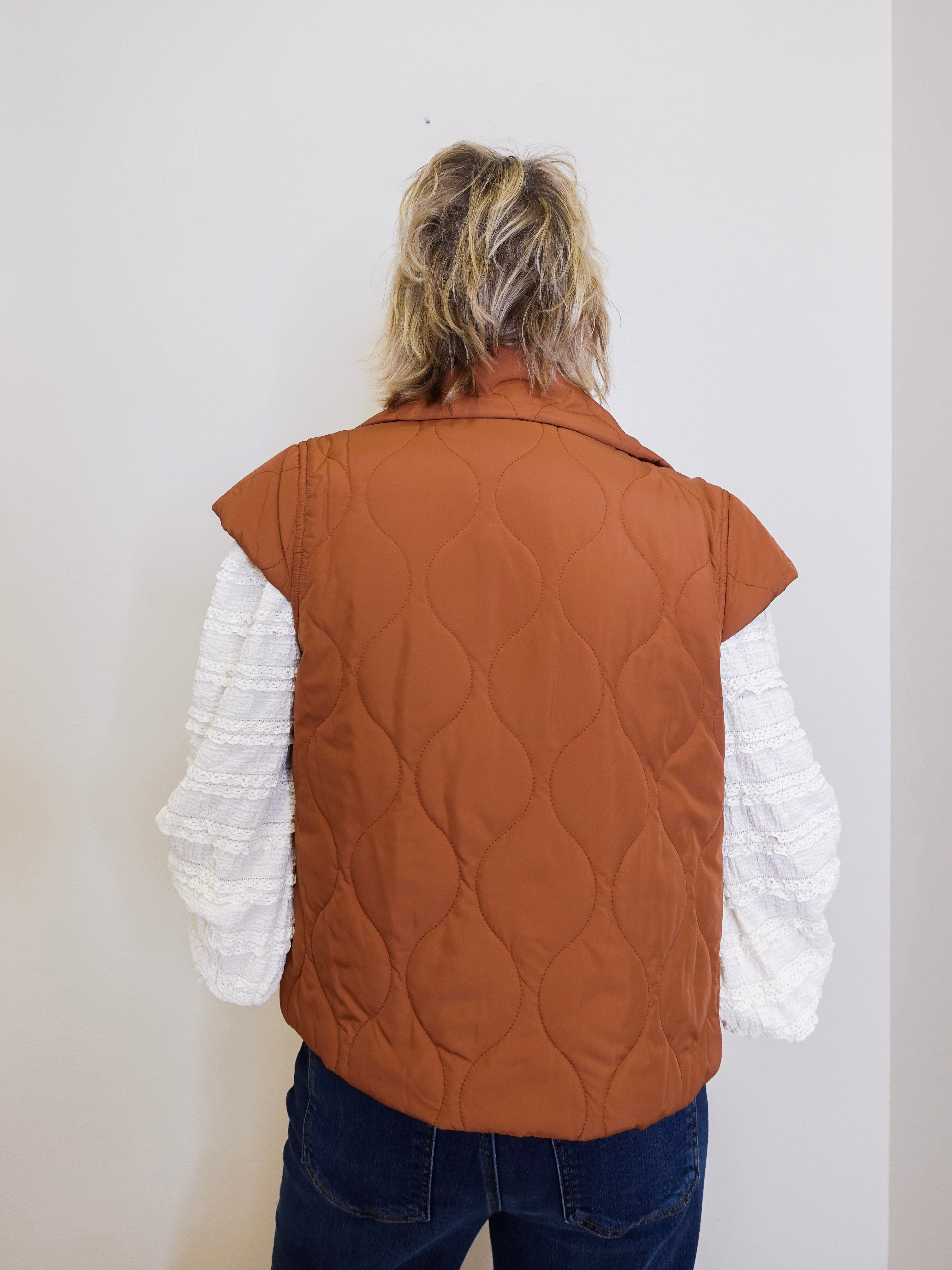 Person wearing a brown quilted vest over a white long-sleeve shirt against a plain background