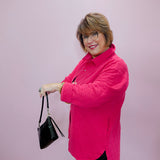 Woman wearing a bright pink jacket holding a black handbag against a light pink background