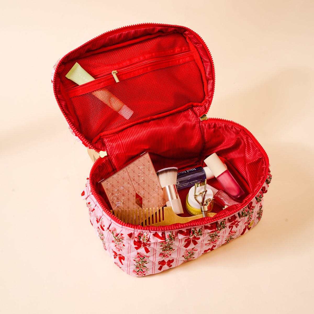 Open red cosmetic bag with floral base containing various items on a beige background